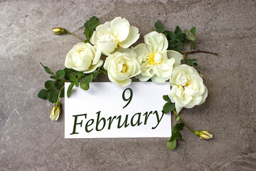 February 9th. Day 9 of month, Calendar date. White roses border on pastel grey background with...