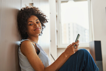 Pleased African American woman with her smartphone looking ahead