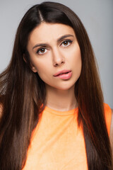 Naklejka premium pensive young woman biting lip and looking at camera isolated on grey