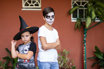Caucasian boy and girl posing with their costumes at the entrance of their house. Halloween celebration concept.
