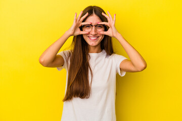 Young caucasian woman isolated on yellow background showing okay sign over eyes