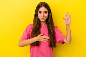 Young caucasian woman isolated on yellow background taking an oath, putting hand on chest.