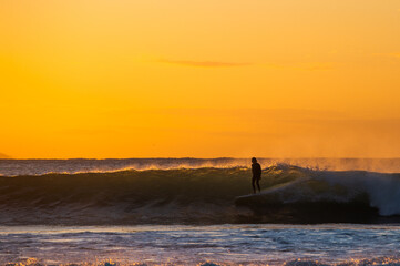 Surfer rides a wave during sunrise