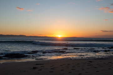 The sun rises over the ocean as waves break in the foreground