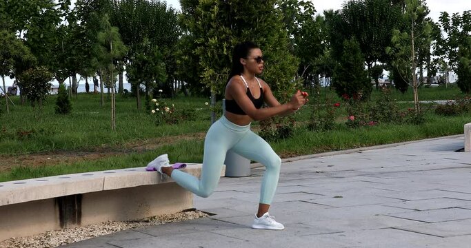 Young fit sporty black African woman in top and leggings does leaning forward exercise working out outdoor on summer. Sport, fitness training, active healthy lifestyle, stretching, warm up concept.