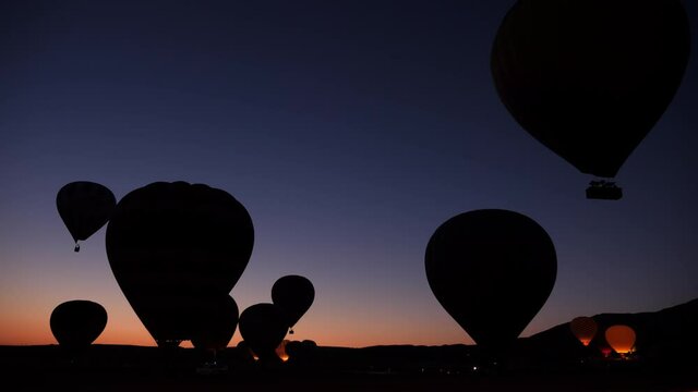 Silhouettes of hot air balloons flying up in the early morning at sunrise