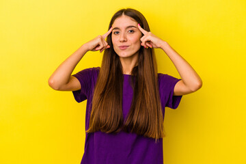 Fototapeta na wymiar Young caucasian woman isolated on yellow background focused on a task, keeping forefingers pointing head.