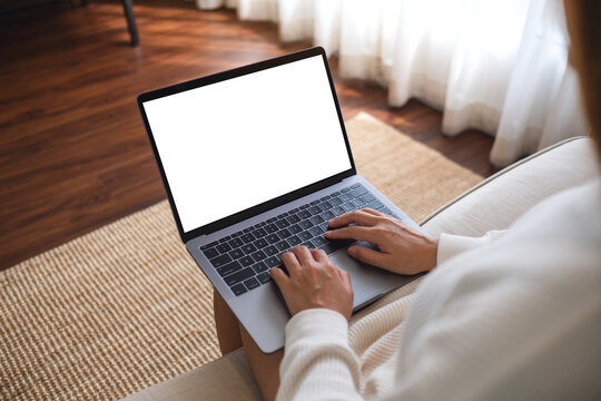 Mockup image of a woman working and typing on laptop computer with blank screen while sitting on a sofa at home