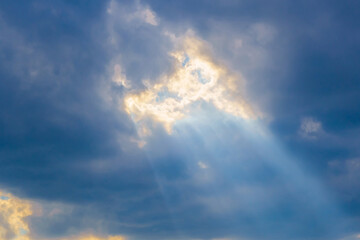 Sun's rays break through low dark clouds. Hole in clouds looks like it was burned by sun