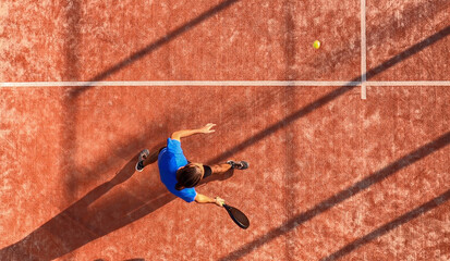 Top view of a man hitting a ball with the racket to practice paddle tennis.