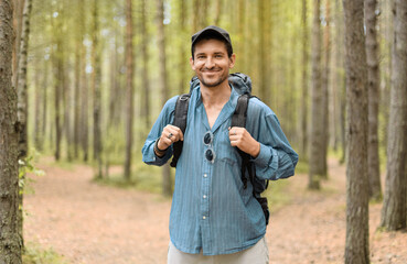Naklejka na ściany i meble Smiling man, 40 years old, with his tourist backpack is standing in a forest.