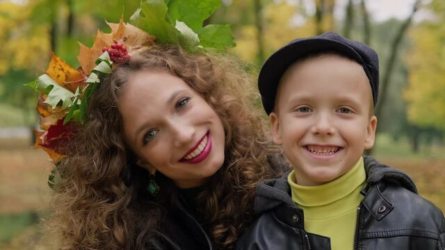Happy family in autumn park hugging. Mother with her little son having fun outdoors. Motherhood concept. Mother with wreath in hair enjoying day with son. Close up in 4K, UHD