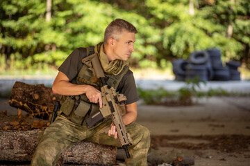 A man sitting with an airsoft assault rifle in military uniform in concrete hangar