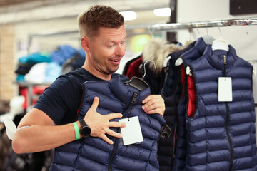 Man tries on warm vest in store closeup