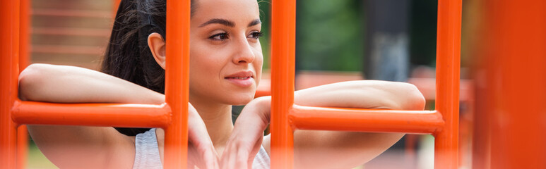 happy sportswoman looking away near orange vertical ladder outside, banner