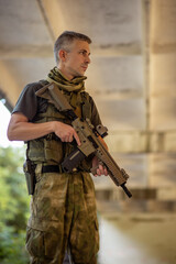 A man standing with an airsoft assault rifle in military uniform in concrete hangar