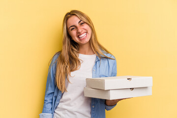 Young caucasian blonde woman holding pizzas isolated on yellow background  happy, smiling and cheerful.