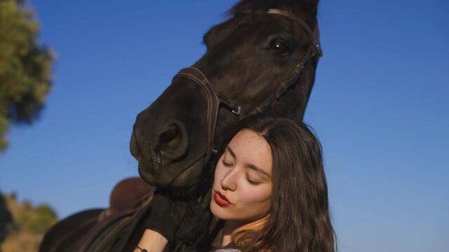 Close-up head of graceful horse with slim beautiful equestrian talking hugging mammal. Purebred stallion and Caucasian woman with pierced nose and with Russian Happiness tattoo at background of sky
