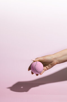Hand holding pink tennis ball on the pink background. Female sport concept