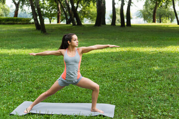 young woman standing in warrior pose on yoga mat in park