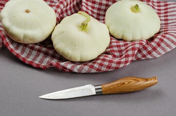 Three Pattypan squash, a knife, and a red checkered napkin on a gray background. Raw wholesome white fruit rich in fiber. Healthy Eating.