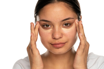 Head shot of a young beautiful woman applies concealer under her eyes