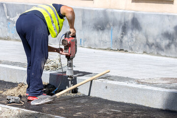 A worker makes a hole in the asphalt with a perforator in order to install a road sign. Road works.