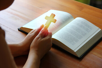 woman holding wood cross in hand praying for god protection with bible