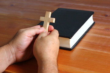 man holding wood cross in hand praying for god protection with bible