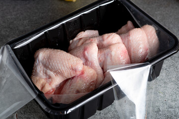 Fototapeta na wymiar Raw chicken wings in plastic wrap on the kitchen table.