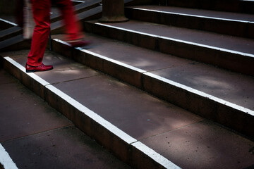 pedestrian in red trousers walks down stairs - motion blur close up on the legs