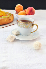 Cup of tea with golden print, coconut candies, peaches and fruit cake on a table
