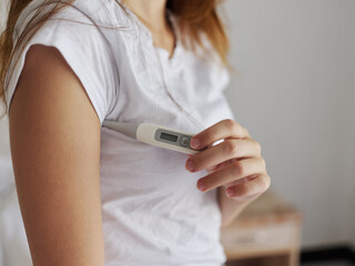 woman in white t-shirt hold thermometer armpit temperature