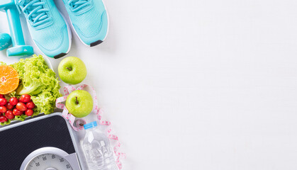 Healthy lifestyle, food and sport concept. Top view of sport shoes, weight scale measuring tape, blue dumbbell, sport water bottles, fruit and vegetables on white wooden background.