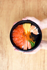 Japanese Rice with Salmon and Tobiko in a bowl holding by hand on wooden background