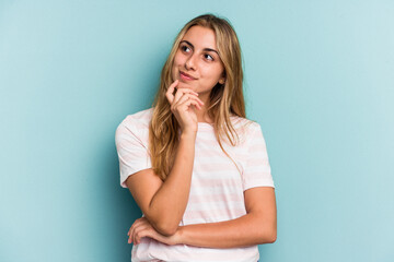 Young caucasian blonde woman isolated on blue background  looking sideways with doubtful and skeptical expression.