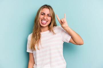 Young caucasian blonde woman isolated on blue background  showing a horns gesture as a revolution...