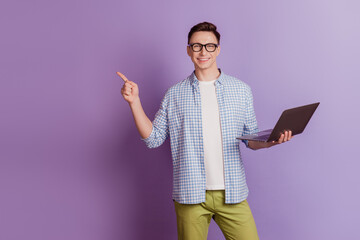 Portrait of cheerful positive guy hold laptop indicate forefinger blank space on violet background