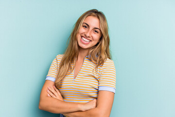 Young caucasian blonde woman isolated on blue background  who feels confident, crossing arms with determination.