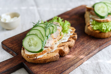 Sandwiches with chicken meat, cucumber, lettuce  and soft cheese on wooden board. Selective focus