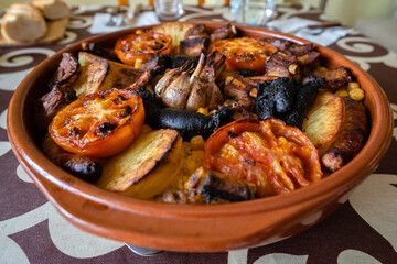 Ceramic pot with dry cooked rice with tomatoes, chickpeas, potatoes, garlic and sausages on a white background. Baked Rice, Valencia.
