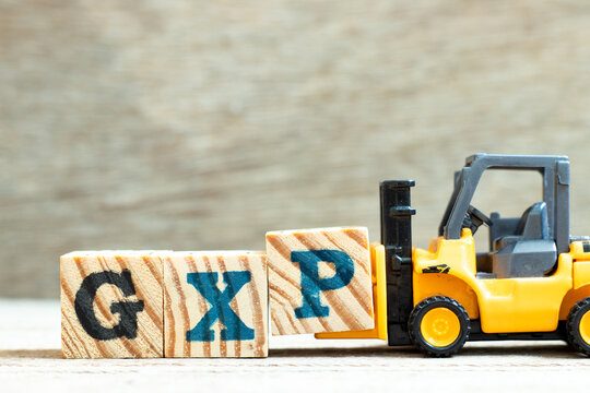 Toy forklift hold letter block P to complete word GXP on wood background