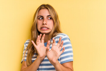 Young caucasian blonde woman isolated on yellow background  rejecting someone showing a gesture of...
