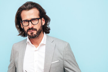 Portrait of handsome confident stylish hipster lambersexual model with long hair.Sexy modern man dressed in elegant suit. Fashion male in spectacles posing in studio near blue wall. Long haired