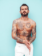 Fototapeta premium Portrait of handsome confident stylish hipster lambersexual model. Sexy modern man. Naked torso with tattoos.Fashion male posing in studio near light blue wall
