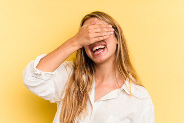 Young caucasian blonde woman isolated on yellow background  covers eyes with hands, smiles broadly waiting for a surprise.
