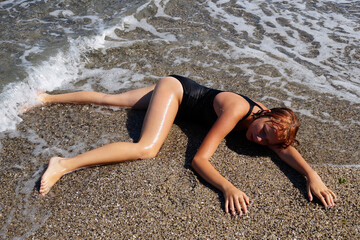 teen girl sunbathes on wet sand near the water on the beach