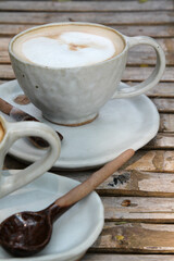 Hot coffee cappuccino in white ceramic cup and spoon on bamboo table.