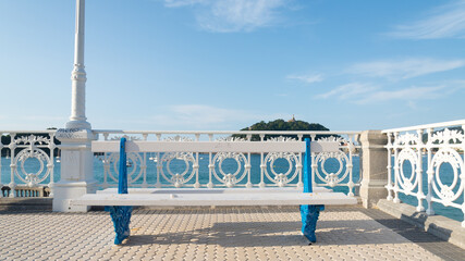 Naklejka premium Bench on the promenade of San Sebastian, Spain. Blue sky with white clouds on the background.