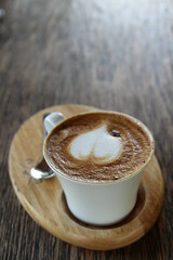 Hot coffee cappuccino in white ceramic cup on wooden tray.